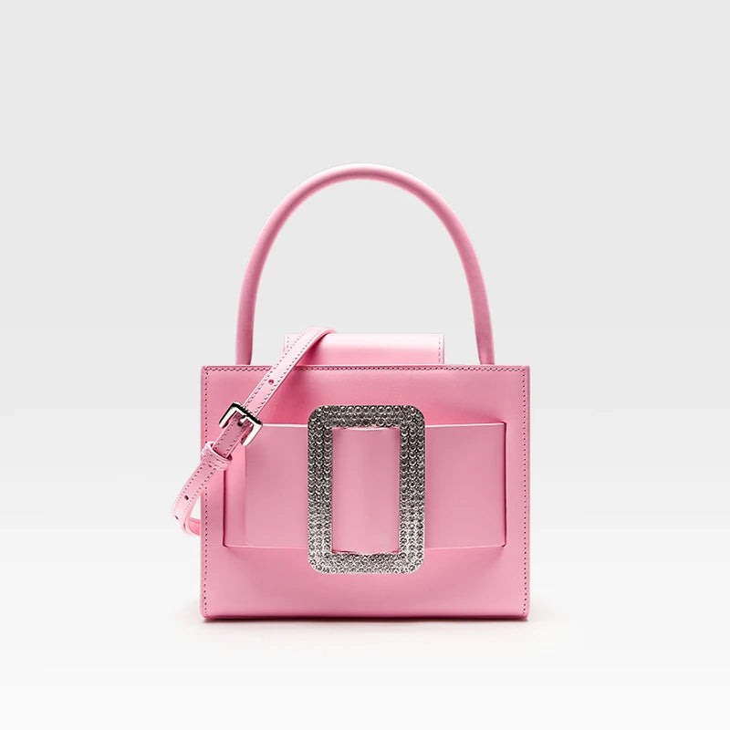 Pink handbag with a decorative silver buckle on a light gray background,