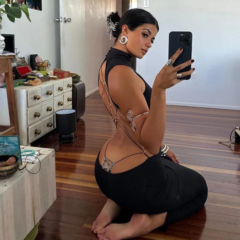 Woman taking a mirror selfie in a black dress with intricate designs, sitting on a wooden floor in a room.