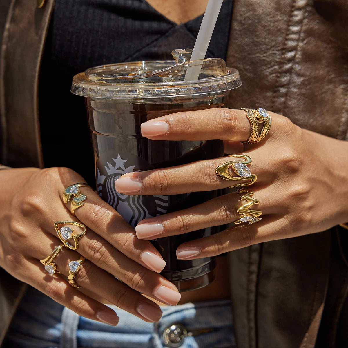 Person holding a Starbucks cup with multiple gold rings on fingers
