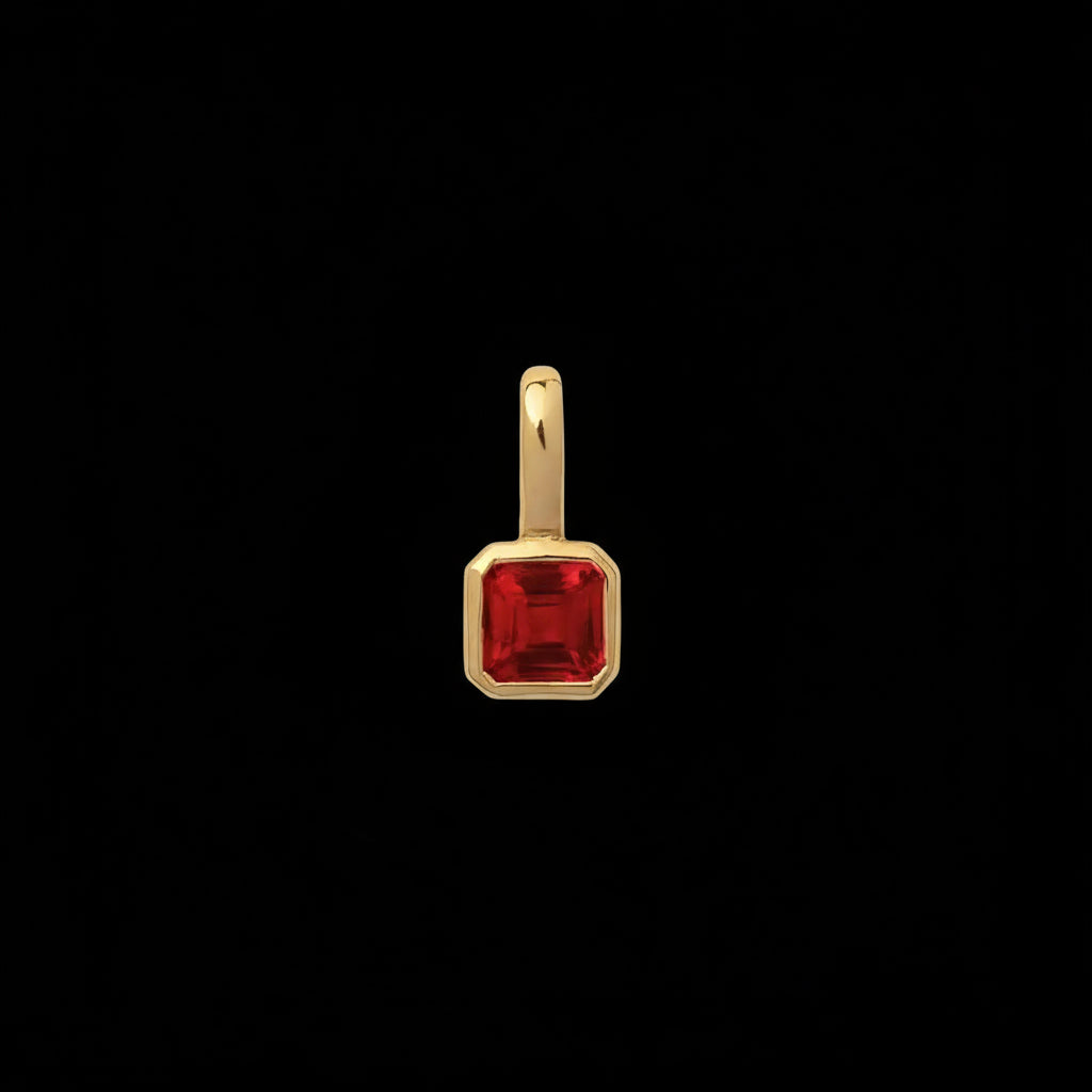 Gold pendant with a red gemstone on a beige background