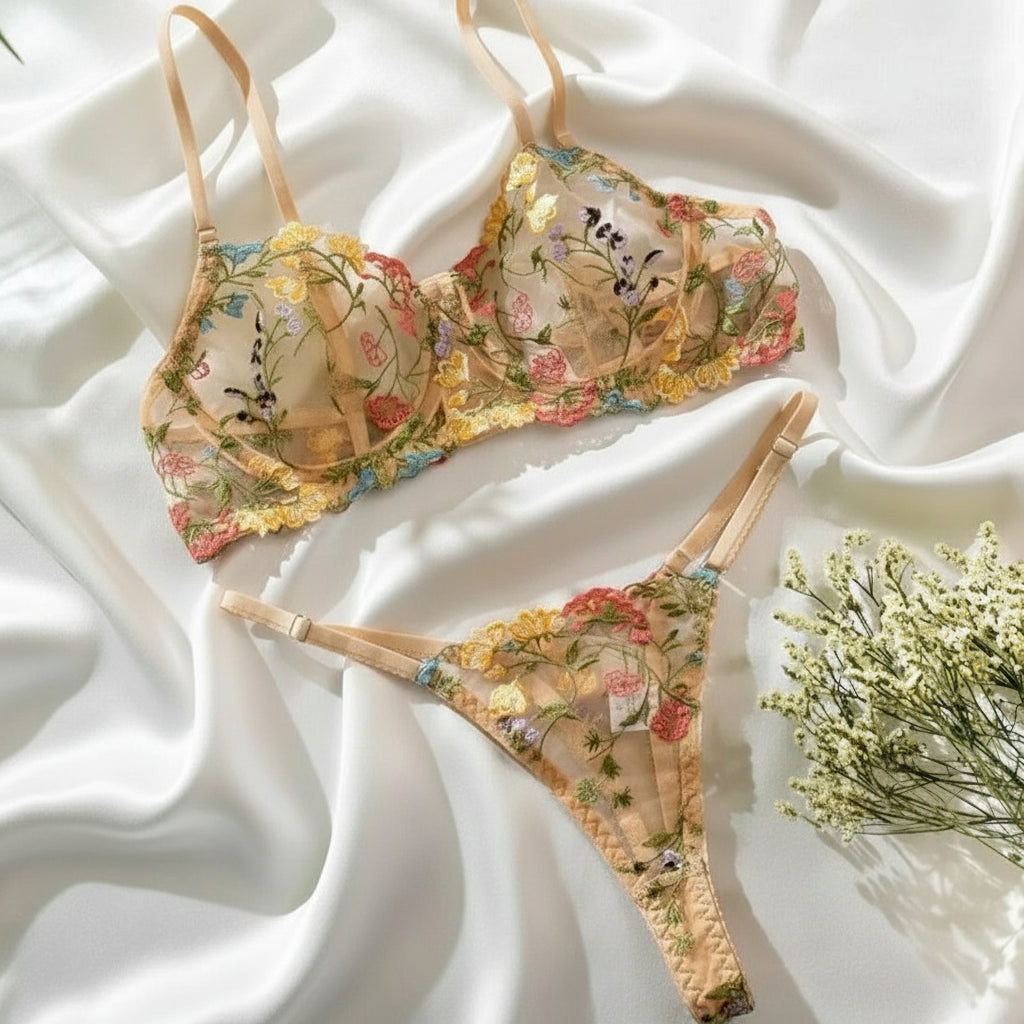 Floral embroidered lingerie set on a white fabric background with a plant and dried flowers.