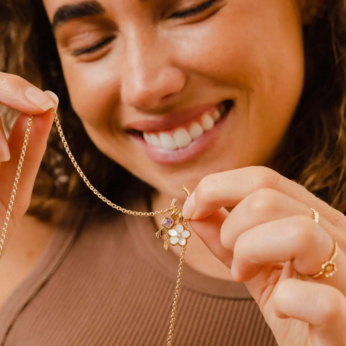 Woman holding a gold necklace with a pendant, smiling.