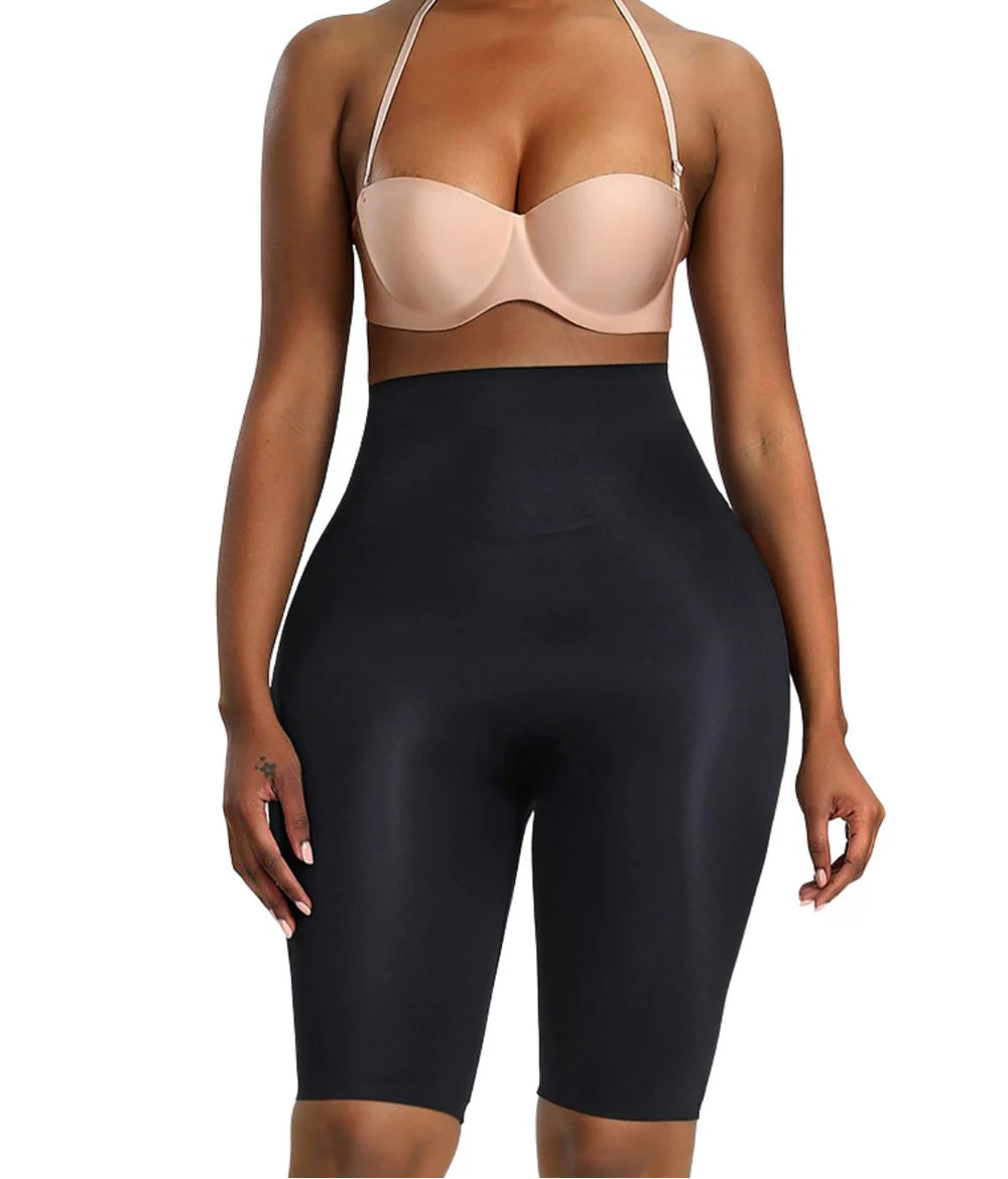 Woman wearing a beige bra and black shapewear shorts on a white background